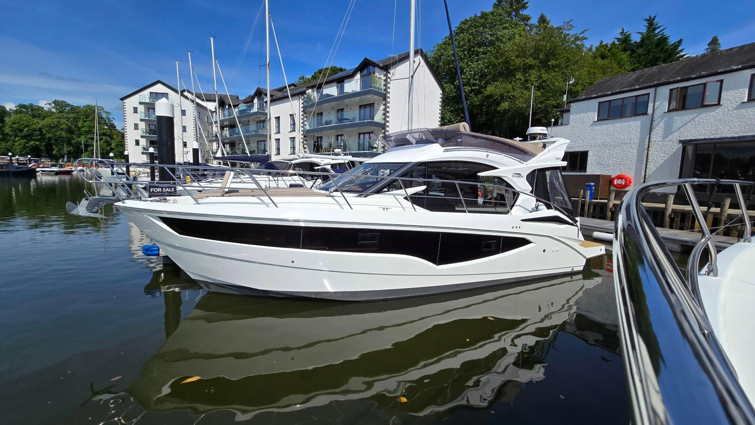 2025 Galeon 360 Fly yacht docked at marina, surrounded by modern buildings and clear blue sky.
