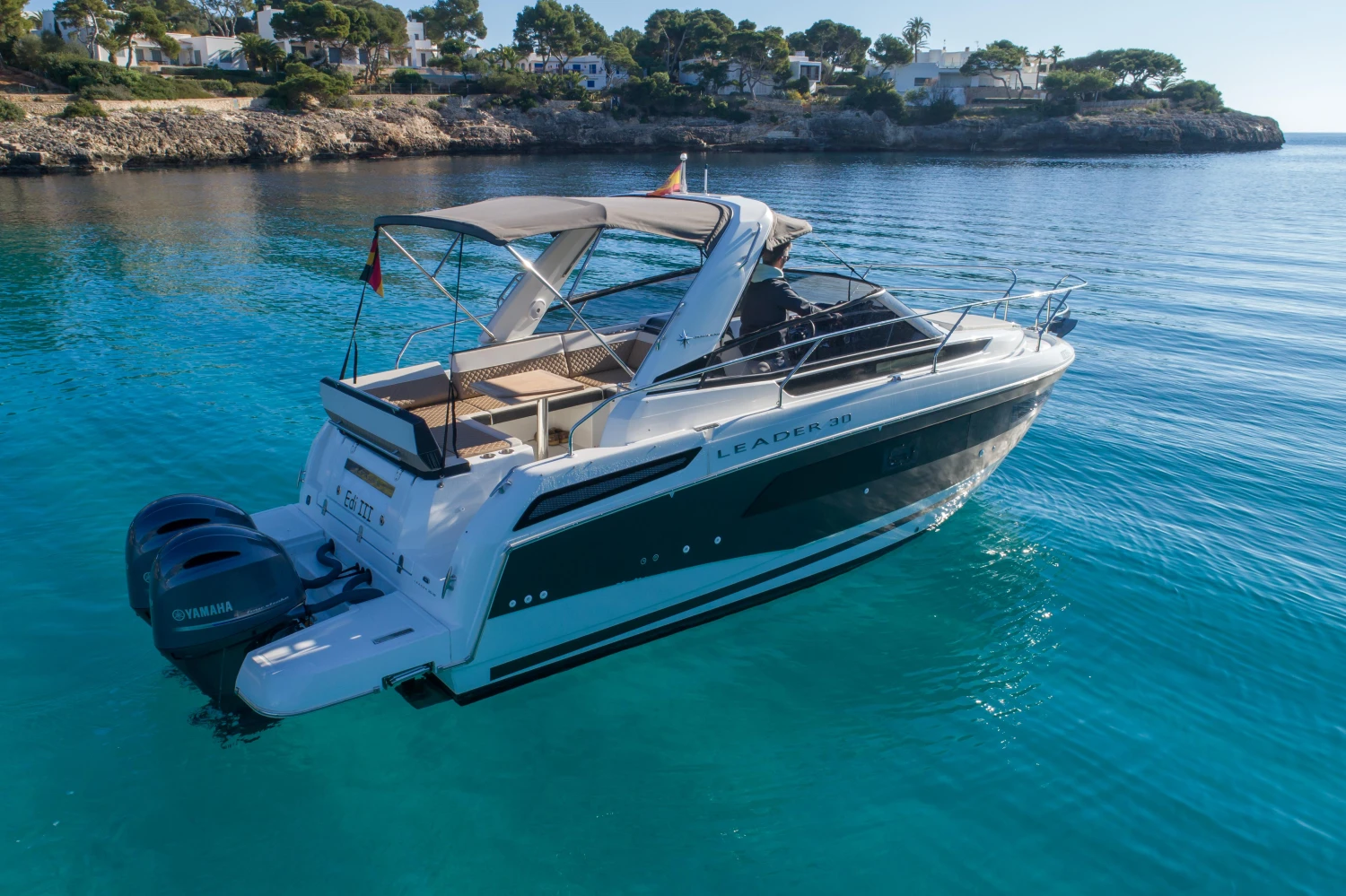 2018 Jeanneau Leader 30 yacht on clear blue water near rocky shoreline.