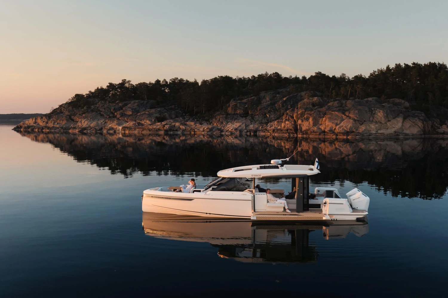 2025 Saxdor 400 GTO yacht on serene water with rocky shoreline backdrop at sunset.